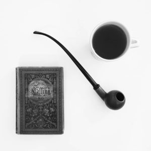 Eine Lesepfeife zusammen mit einem alten Lessingbuch und einer Tasse Kaffee. Heller Hintergrund, Bild in schwarzweiß.